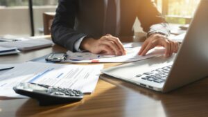 Person arbeitet konzentriert mit Laptop und Unterlagen am Schreibtisch.